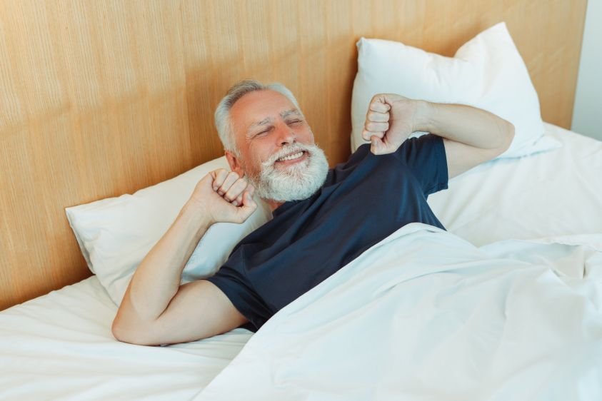 Happy bearded senior man stretches, wake up lying on comfortable bed2e00 Morning concept 